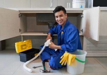 cheerful asian plumber sitting floor repairing kitchen sink 1098 17780